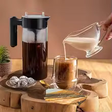 Lait versé dans un café devant une cafetière infusion à froid sur planche